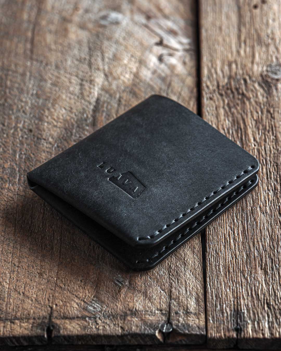 Handmade leather bi-fold wallet for men. Minimalist and rugged style. Traveler's wallet black front